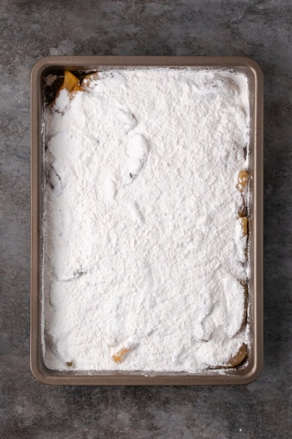 Apple pie filling topped with boxed cake mix in a baking pan.