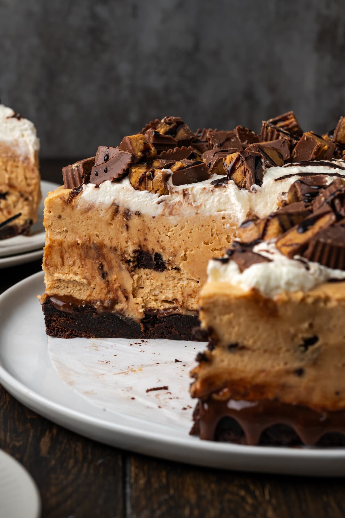 Brownie cheesecake topped with peanut butter cups on a white plate, with a slice missing.