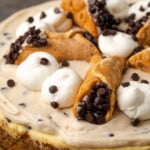 Cannoli cheesecake decorated with swirls of whipped cream and mini cannoli pastries.