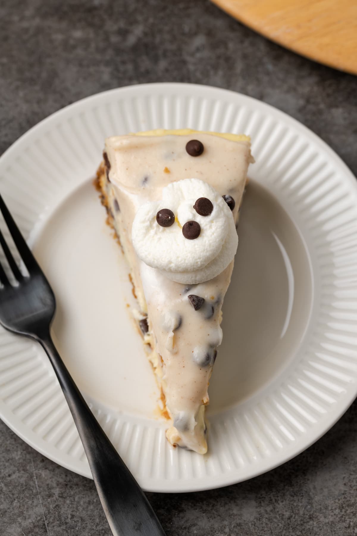 A slice of cannoli cheesecake topped with a swirl of whipped cream on a white plate next to a fork.