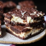 Two Cheesecake Brownies Stacked on a Plate With a Bite Taken From the Top One