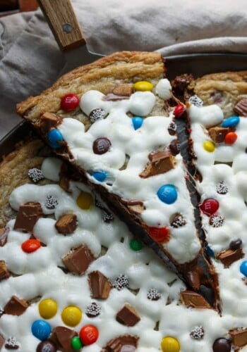 A slice of chocolate chip cookie pizza topped with melted marshmallows, M&Ms, and chopped peanut butter cups