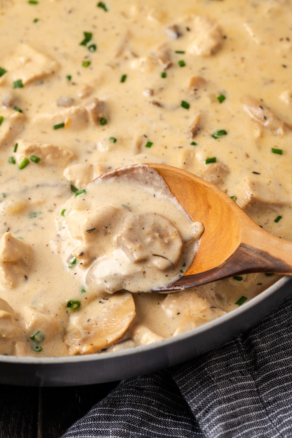 Close up of cream of mushroom chicken in a skillet with a wooden spoon.