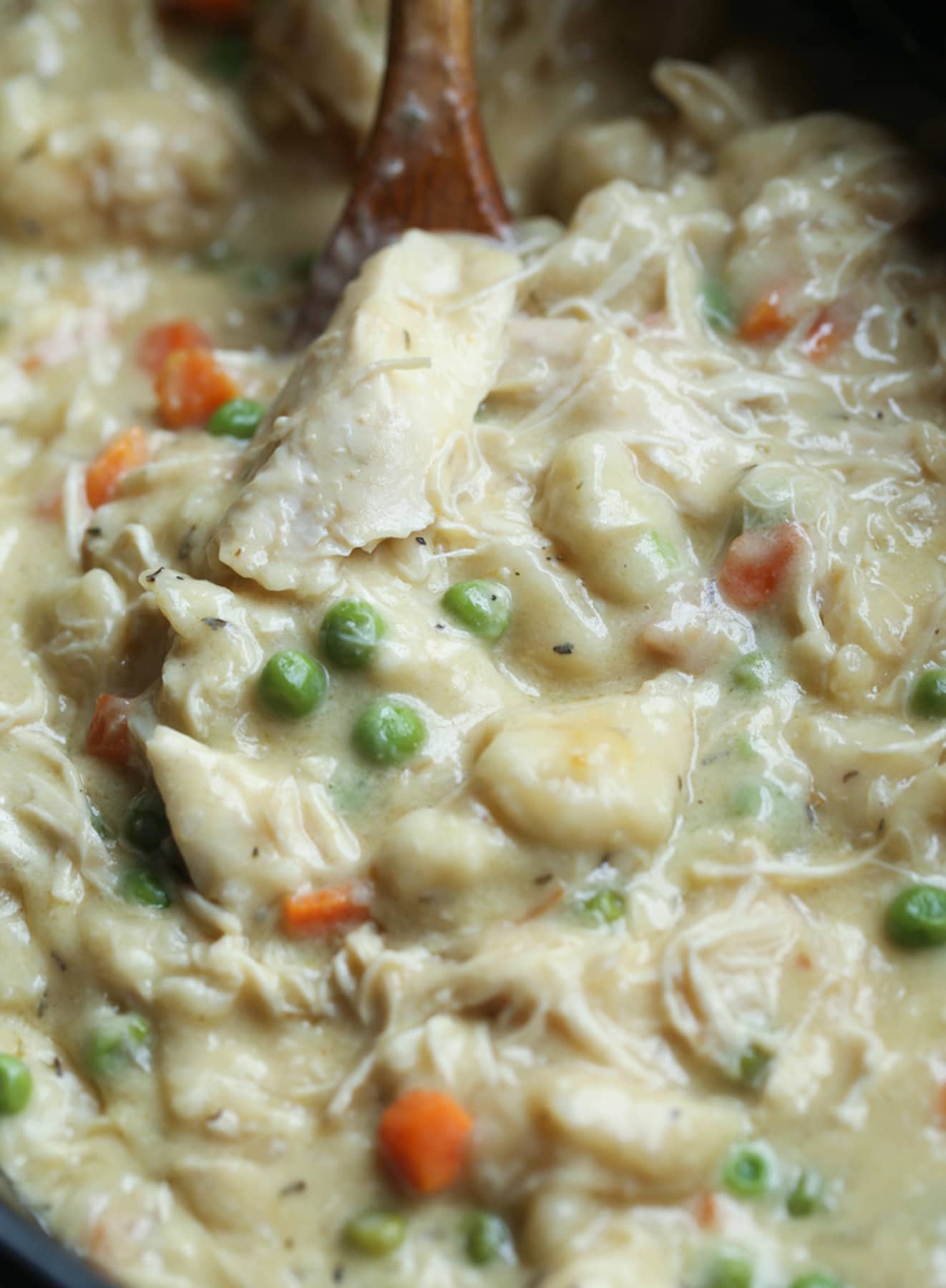 Spooning out chicken and dumplings in a Crock Pot with shredded chicken, carrots, and peas