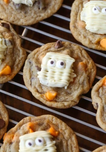 Pretzel mummies on top of a chocolate chip cookie with orange chips.