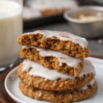 A stack of iced oatmeal cookies on a white plate, with the top cookie broken in half.