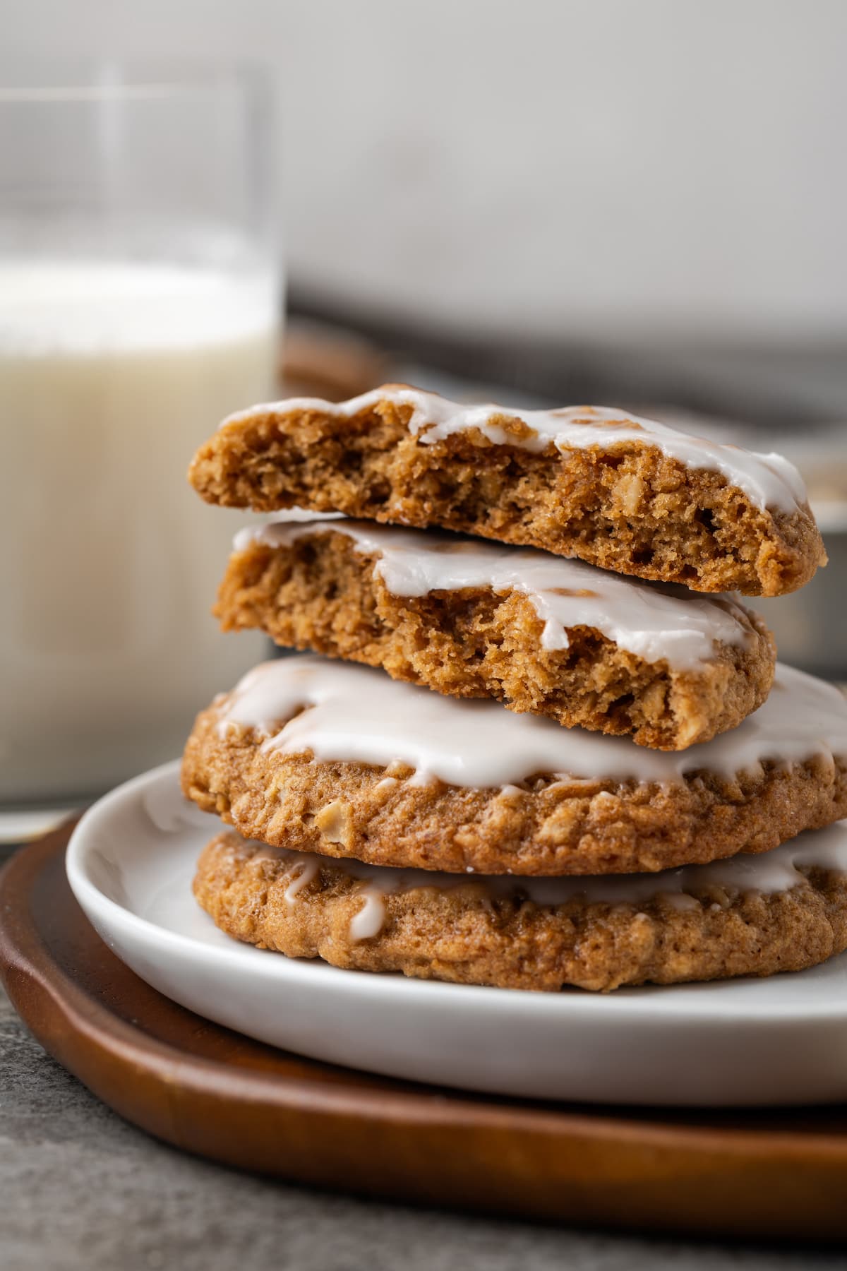 A stack of iced oatmeal cookies on a white plate, with the top cookie broken in half.