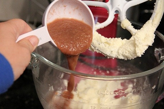 Applesauce being poured into a mixing bowl of batter