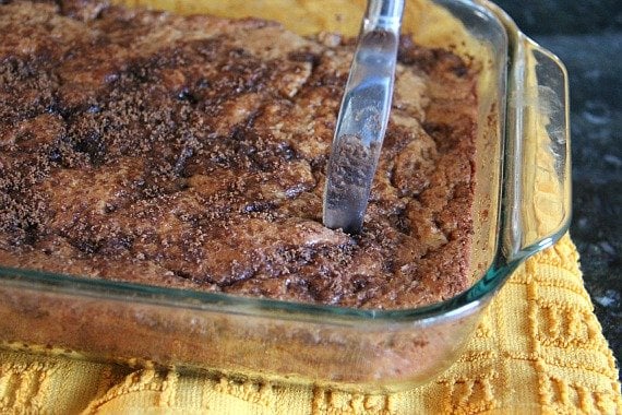 Apple fritter cake in a baking dish being cut with a butter knife