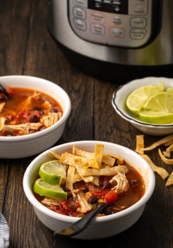 A bowl of chicken tortilla soup garnished with lime wedges and crispy tortilla strips, with a bowl of lime wedges in the background next to the Instant Pot.