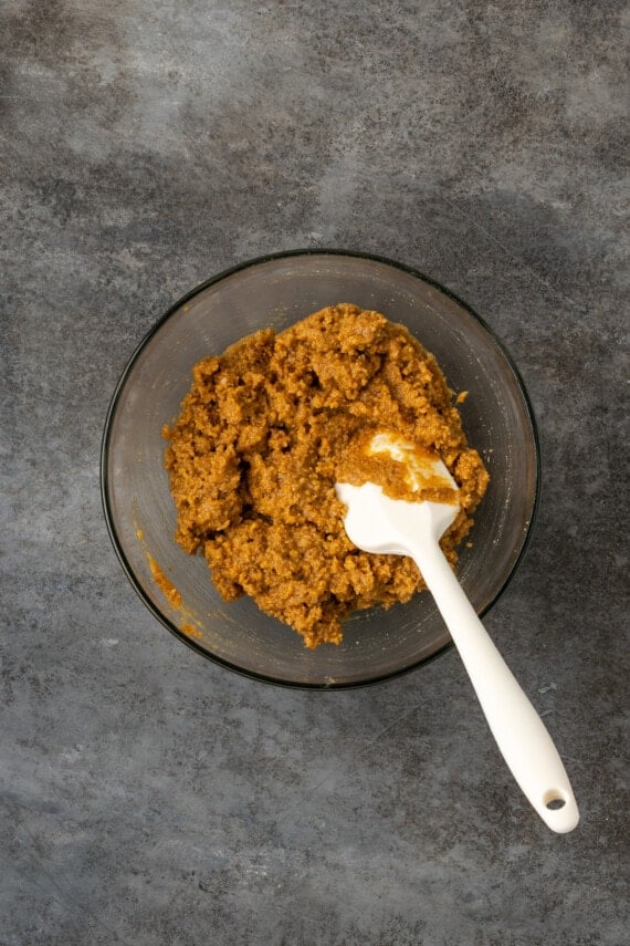Graham cracker crust mixture in a glass bowl with a rubber spatula.