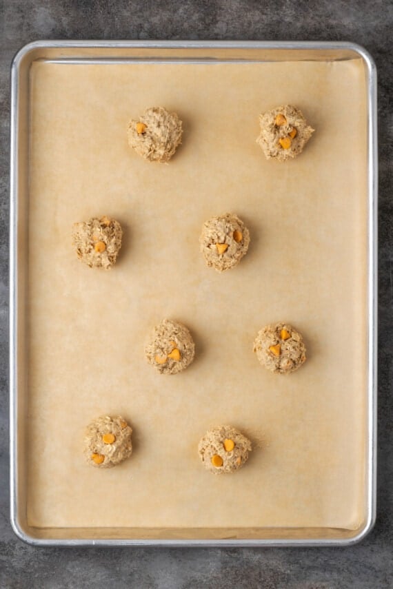 Oatmeal butterscotch cookie dough balls on a parchment-lined baking sheet.