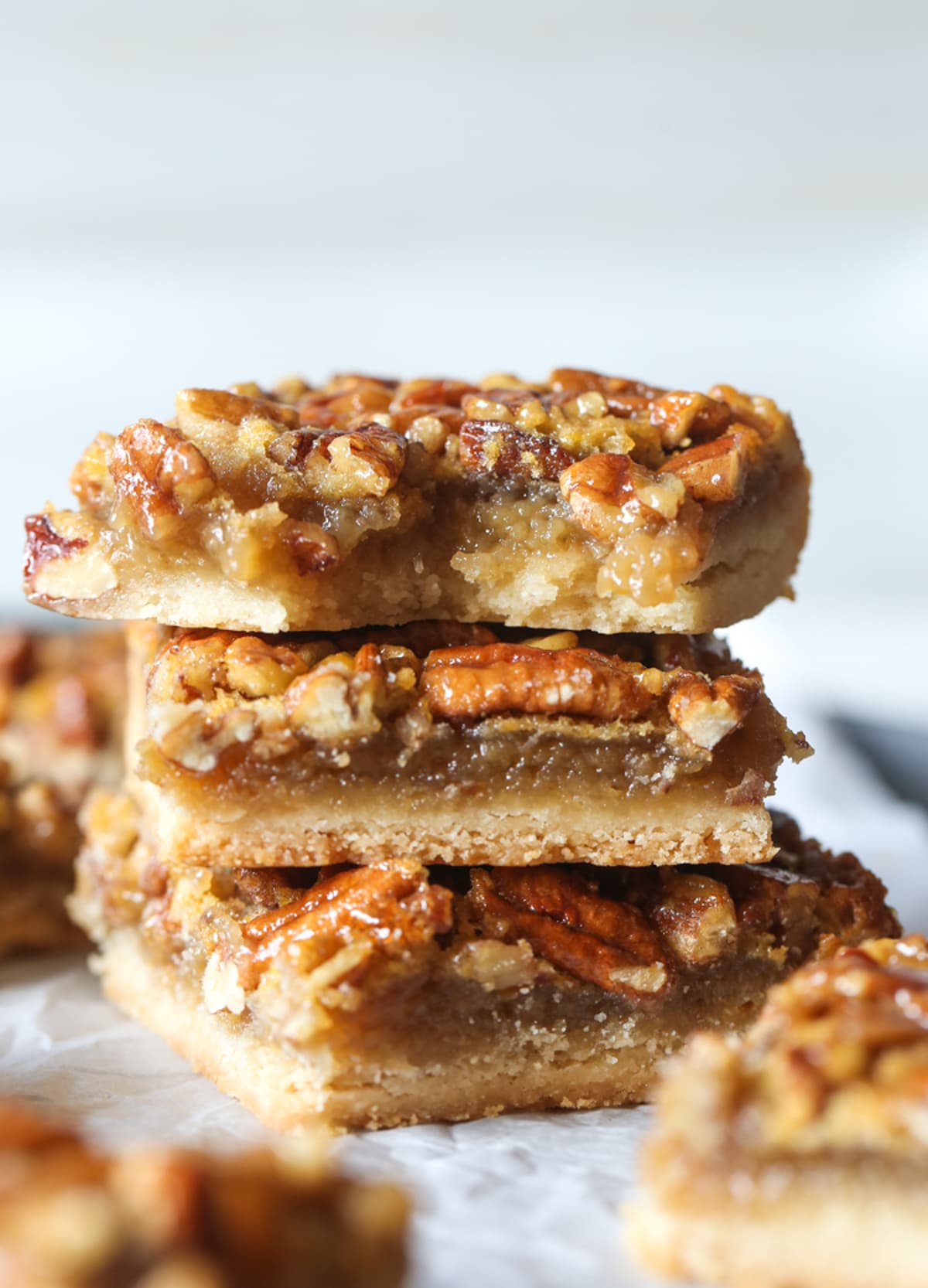 Three stacked Pecan Pie Bars showing the shortbread crust layer, the filling and nuts layers with a bite taken from the bar on top.