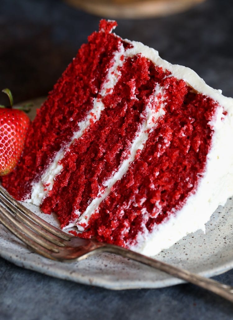 A slice of three layer red velvet cake with frosting.