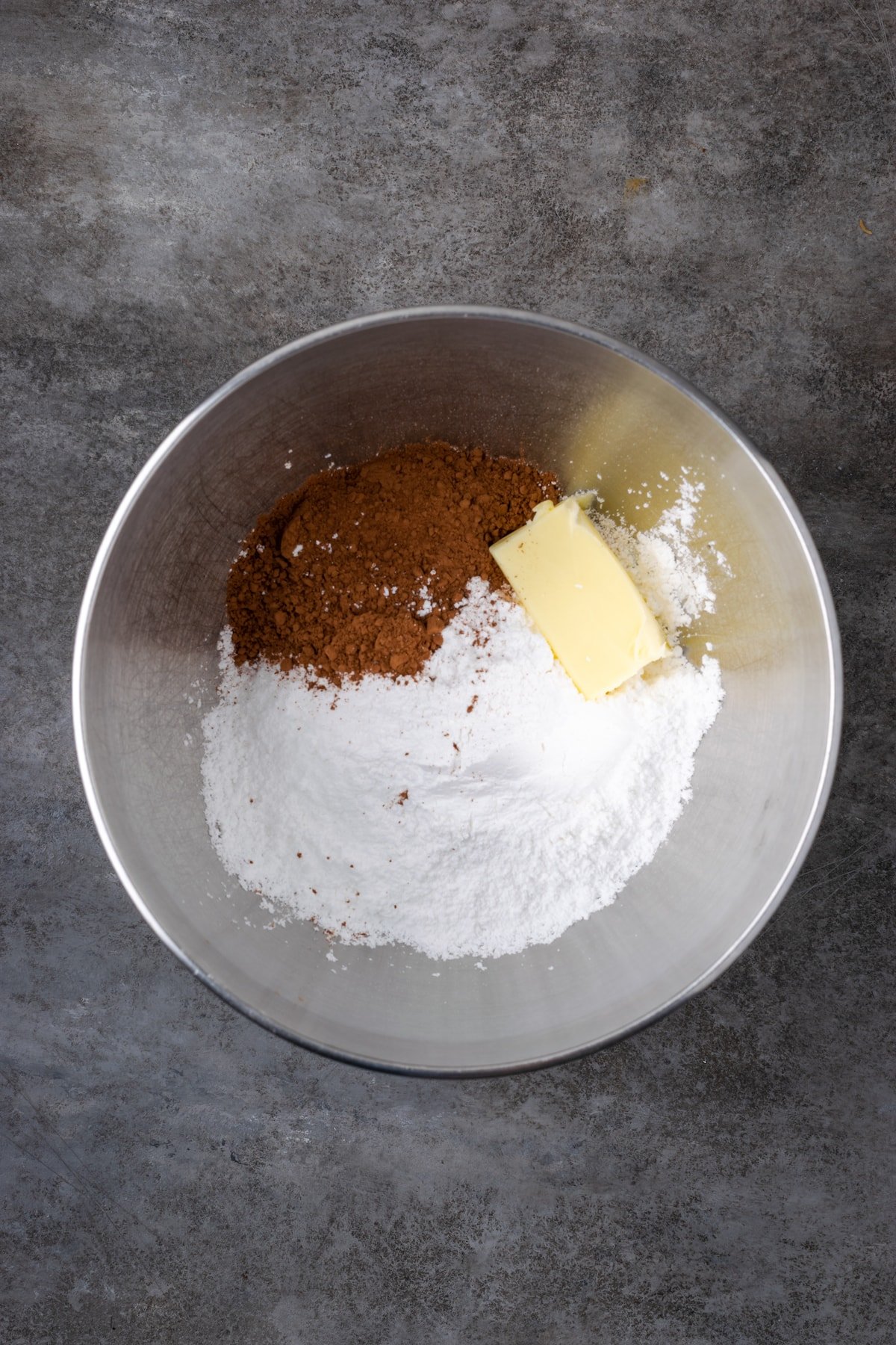 Butter, cocoa, and powdered sugar combined in a mixing bowl.