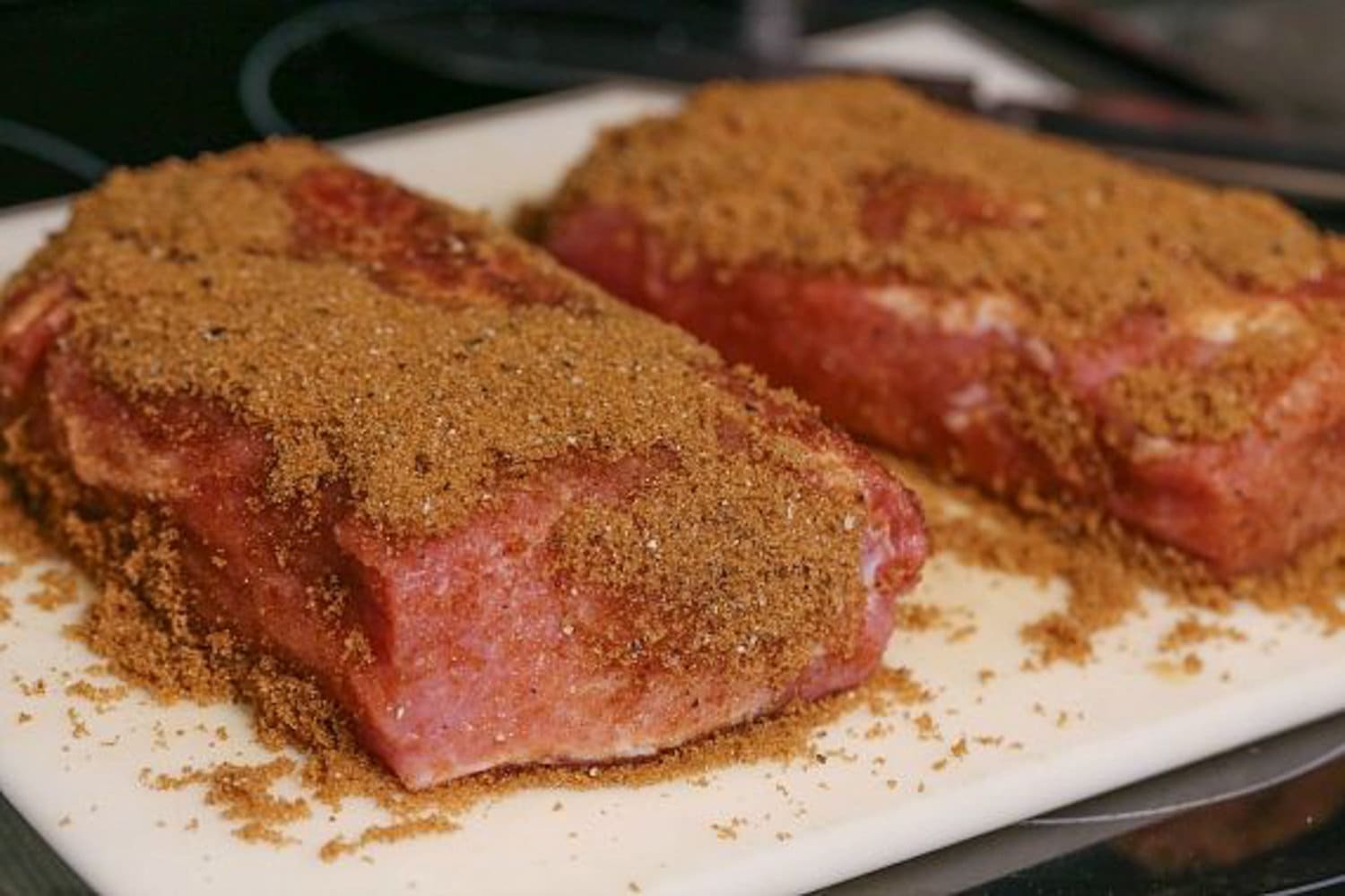 Pork roast topped with dry rub on a white cutting board