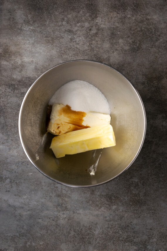 Cream cheese, butter, and sugar combined with vanilla in a metal mixing bowl.